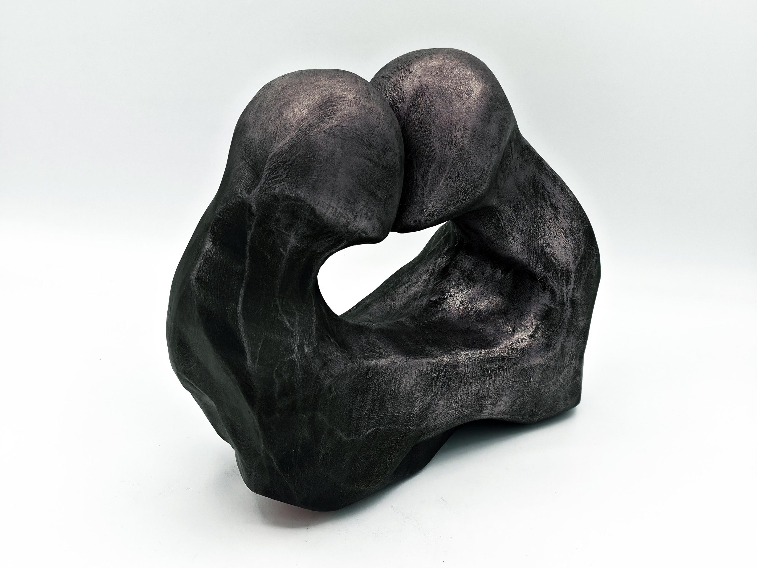Dark textured sculpture of two hands interlocking to form a loop against a light background, conveying connection or unity.