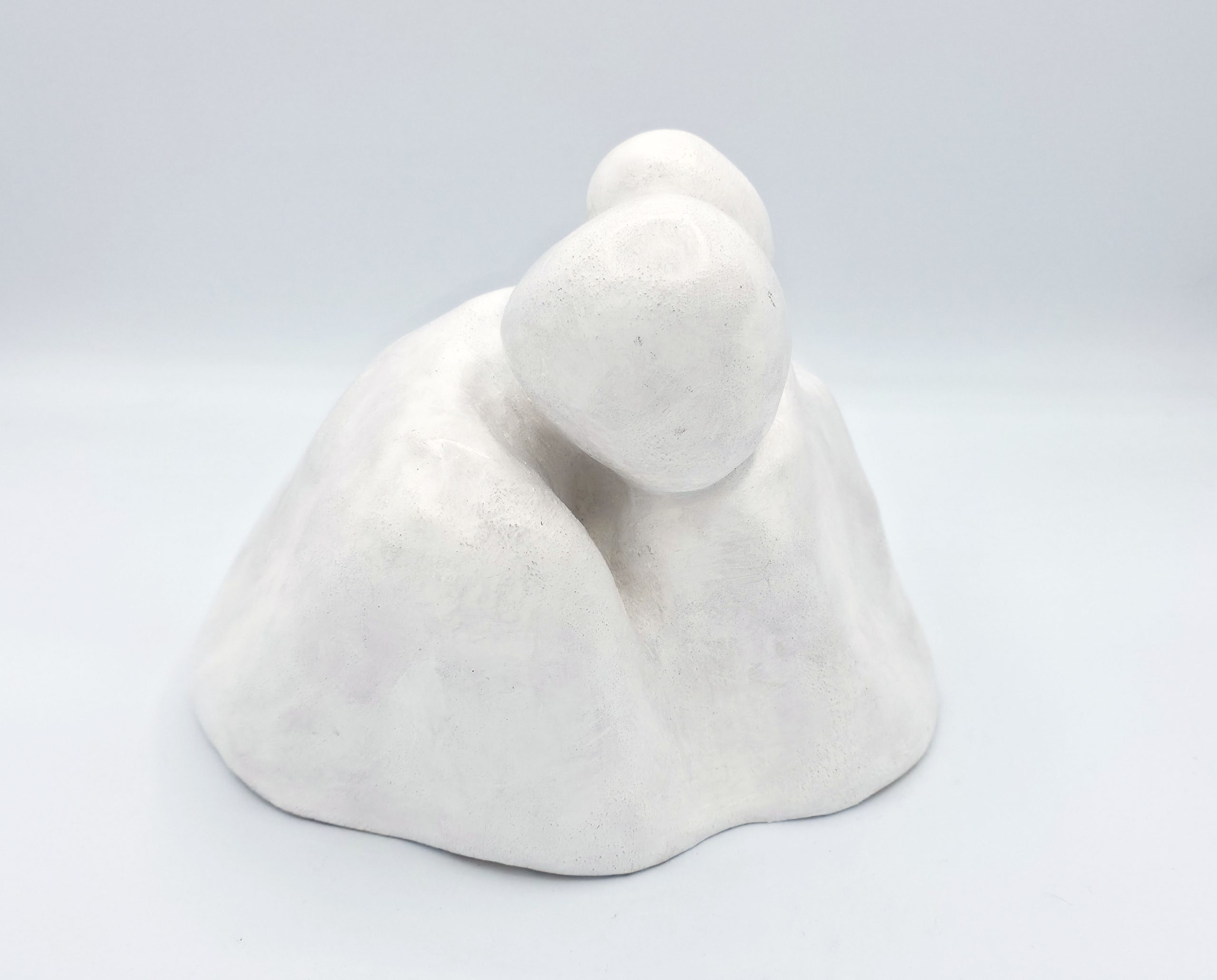 Close-up of a white stone sculpture resembling stacked rounded fingers against a pale blue sky background.